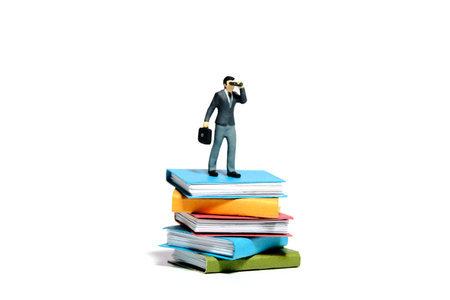 Miniature tiny people toy figure photography. Business research literature concept illustration. Businessmen using binocular standing above book. Isolated on a white background. Image photoの写真素材