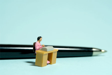 Miniature tiny people toy figure photography. A woman office worker sits at a desk in front of a pen. Image photoの写真素材