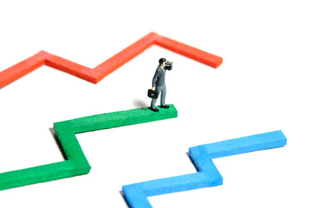 Miniature tiny people toy figure photography. Progress monitoring concept illustration. A businessman using binocular standing above multiple bar chart. Isolated on a white backgroundの写真素材