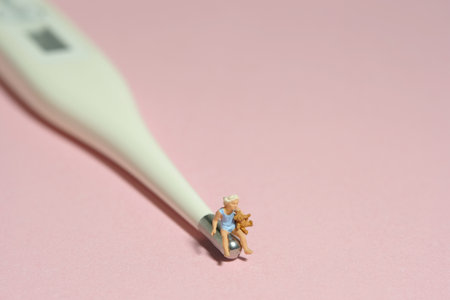 Miniature tiny people toy figure photography. A girl toddler sitting above white thermometer holding teddy bear doll. Isolated on pink background. Image photoの写真素材