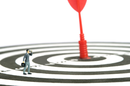 Miniature tiny people toys photography. Business strategy concept illustration. Businessman using binoculars telescope, standing above dartboard. Isolated on white background. Image photoの写真素材
