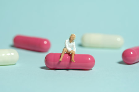 Miniature tiny people toy figure photography. A girl teenager sitting above pink medicine pill....