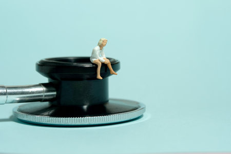 Miniature tiny people toy figure photography. A girl sitting above stethoscope. Isolated on blue background. Image photoの写真素材