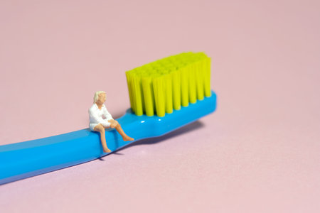 Miniature tiny people toy figure photography. A girl teenager sitting above toothbrush. Isolated on...