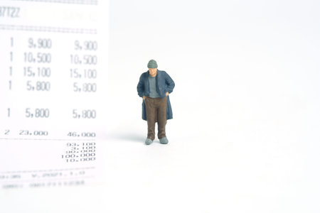 Miniature people toy figure photography. Trouble paying bills concepts. A sad man with no money standing beside receipt of payment. Isolated on white background. Image photoの写真素材