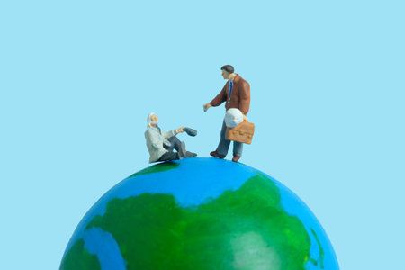Miniature people toy figure photography. Charity day concepts. A businessman giving money to an elderly man above earth globe with blue background. Image photoの写真素材