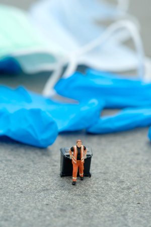 Miniature people toy figure photography. Cleaning worker with trash bin walking between used rubber latex gloves on the road. Image photoの写真素材