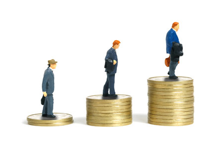 Miniature people toy figure photography. Businessman standing in line climbing up the stairs made from coin pile. Isolated on white background. Image photoの写真素材