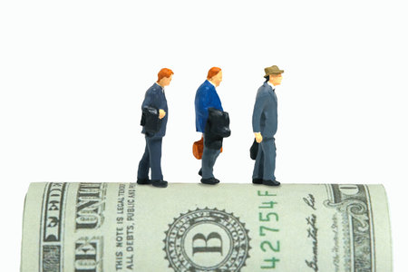 Miniature people toy figure photography. Severance pay for laid off workers concept. Three businessmen with rolled dollar money. Isolated on white background. Image photoの写真素材