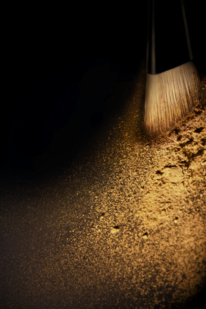 Splash of golden beige cosmetic powder and brush on black background and soft light.の写真素材