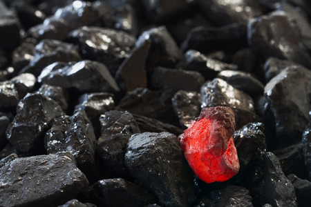 Red hot coal nugget on focus on other cold raw nuggets of coal. Background of raw coals with soft focus exclusion with color and temperature.の写真素材