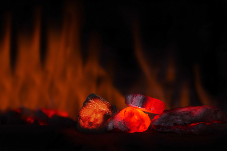 Red hot coal nugget in focus on dark background with flames. Background of raw coals with soft focus exclusion with color and temperature.の写真素材