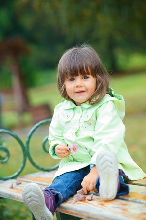 Little girl sitting on a bench in the parkの写真素材