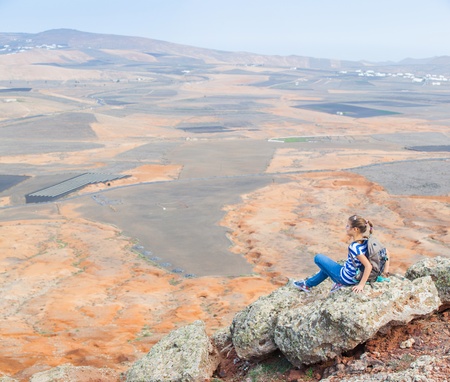 girl sitting on cliff's edge, looking to a sky