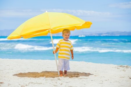 Boy with big umbrella on tropical beachの写真素材