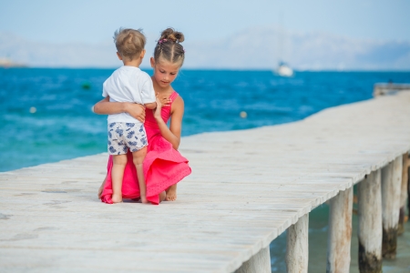Cute toddler boy with his sister walking on jetty with turquoise seaの写真素材