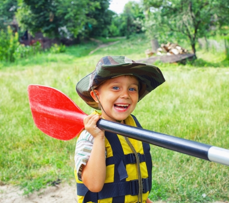 Portrait of happy young boy holding paddle near a kayak on the river, enjoying a lovely summer dayの写真素材