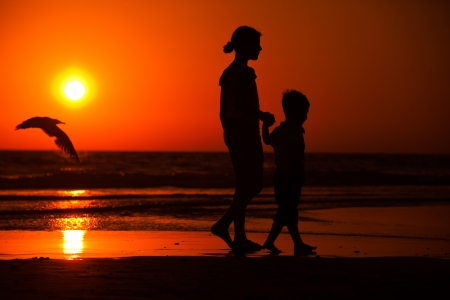 Silhouette of little brother and sister playing at the beach during sunsetの写真素材