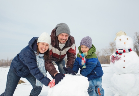 Happy beautiful family building snowman outside in winter timeの写真素材