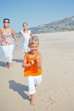 Adorable happy boy with sister and mother running on beachの写真素材