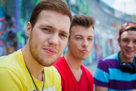 Portrait of happy teens boy with his friends by painted wall looking at cameraの写真素材