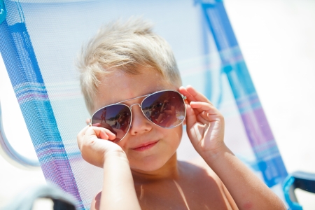Portrait of young boy wearing sunglasses relaxing on beach の写真素材