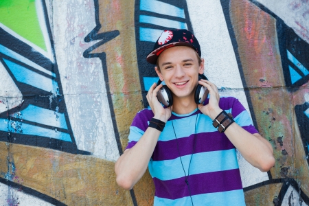 Close-up portrait of happy teens boy with headphones near painted wall listening to musicの写真素材