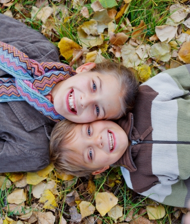 Happy kids lying on autumnal ground covered with dry leavesの写真素材