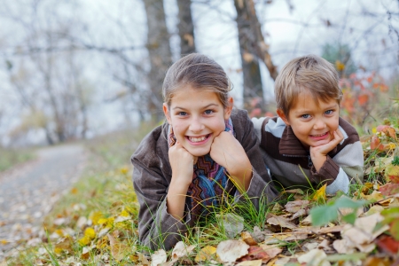 Happy kids lying on autumnal ground covered with dry leavesの写真素材