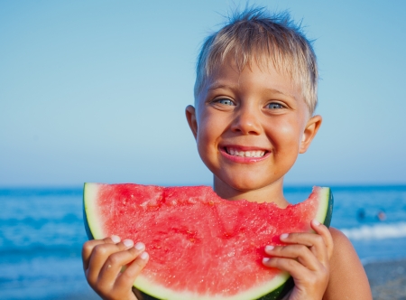 Handsome boy eating slice of watermelon on the beachの写真素材