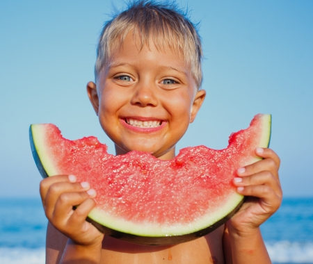 Handsome boy eating slice of watermelon on the beachの写真素材