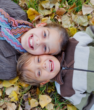 Happy kids lying on autumnal ground covered with dry leavesの写真素材