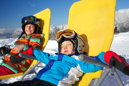 Winter, ski, sun and fun - portrait of kids in winter resort resting in the deck chairの写真素材