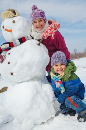Happy beautiful children with snowman outside in winter timeの写真素材