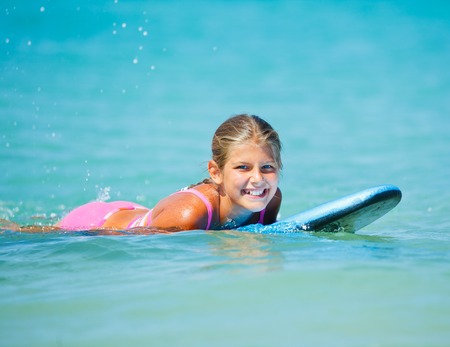 Summer vacation - Happy cute girl having fun with surfboard in the oceanの写真素材