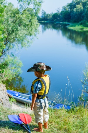 Happy young boy near a kayak on the river, enjoying a lovely summer dayの写真素材