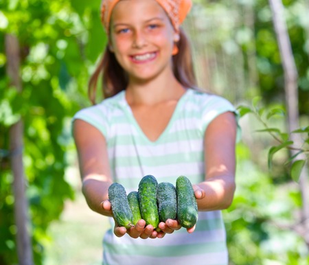 Cute girl with cucumbers in summer garden  Focus on the cucumbers の写真素材
