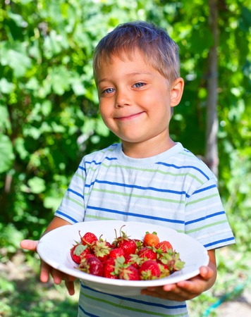 Happy little toddler boy in summer garden with plate of ripe fresh strawberriesの写真素材