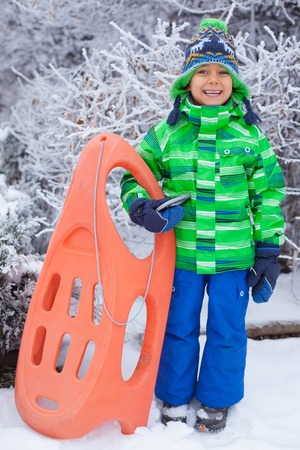 Little boy having fun with sled in winter parkの写真素材