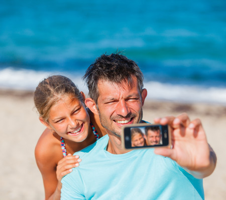 Father and his kids at beach taking selfieの写真素材