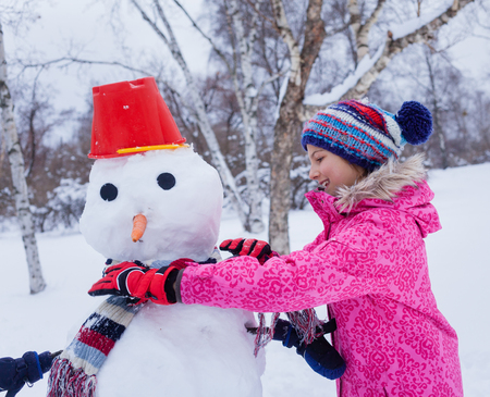 Happy girl having fun in the snow - making snow penguinの写真素材