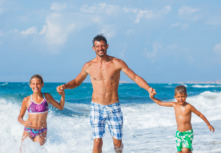Father and his children playing and running on the beach. Concept of friendly family.の写真素材