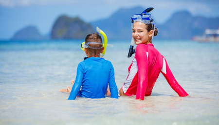 Two happy children on beach with colorful face masks and snorkels, sea in background.の写真素材