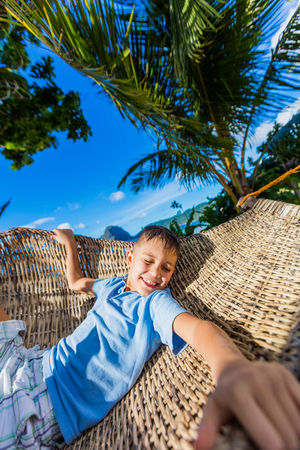 Cheerful little boy relaxing on a tropical beach in hammock.の写真素材
