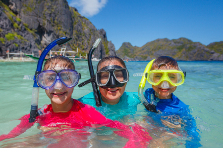 Joyful sister and brother with mother scuba diving in the clear sea.の写真素材