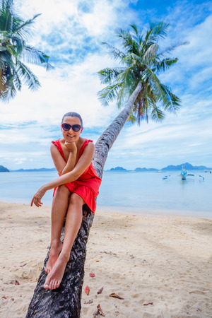 Woman on the beach sitting on palm treeの写真素材