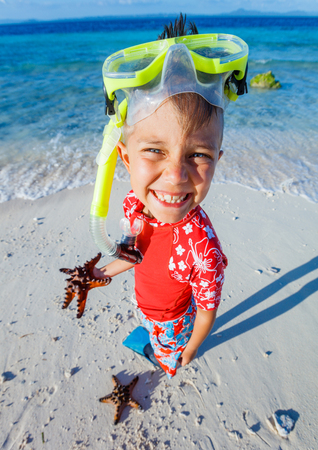 Joyful boy on the tropical beach with equipment to scuba diving and starfish.の写真素材