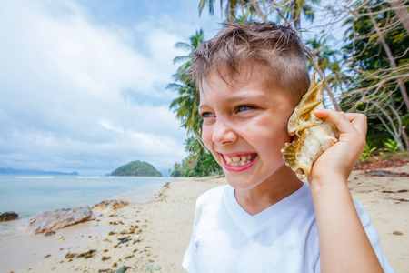 Happy boy with shell listening noise of sea at the tropical beachの写真素材