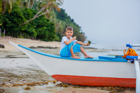 Little boy sitting in boat lying on the beach dreems of the seaの写真素材