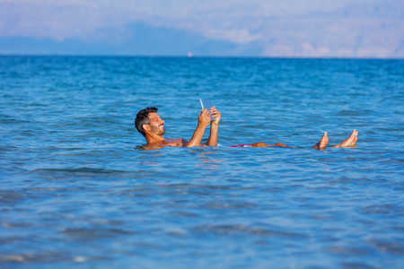 Man floating with the tablet in the waters of the Dead Sea, Israelの写真素材